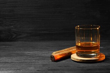 Glass of whiskey and cigars on black wooden table. Space for text