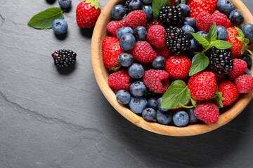 Many different fresh ripe berries in wooden bowl on black table, flat lay. Space for text