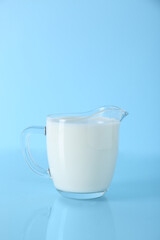 Jug of fresh milk on light blue background, space for text