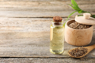 Caraway (Persian cumin) seeds and essential oil on wooden table, space for text