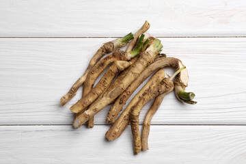 Cut horseradish roots on white wooden table, flat lay