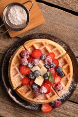 Tasty Belgian waffle with fresh berries, cheese and powdered sugar on wooden table, flat lay