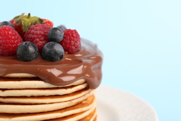 Stack of tasty pancakes with fresh berries and chocolate spread on light blue background, closeup. Space for text