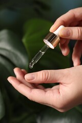 Woman applying cosmetic serum onto hand on blurred background, closeup