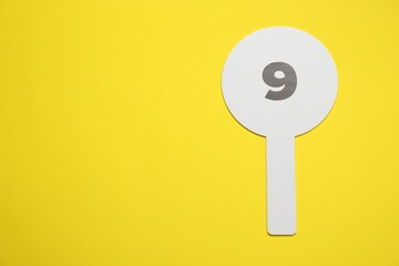 Auction paddle with number 9 on yellow background, top view. Space for text