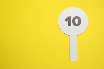 Auction paddle with number 10 on yellow background, top view. Space for text