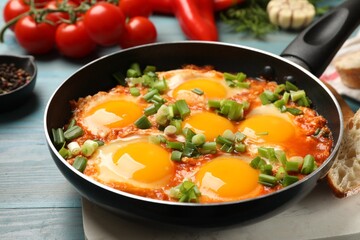 Delicious Shakshuka in frying pan on light blue wooden table, closeup