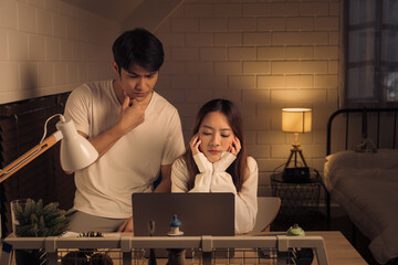 Concerned couple looking at a laptop screen in a softly lit room, both man and woman appears...
