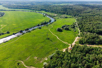 Aerial view of green fields in a river floodplain surrounded by forests