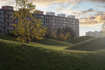 city park in Prague, featuring lush green grassy hills, is illuminated by the warm of sun. apartment buildings painted, real estate and a green living concept in the city.