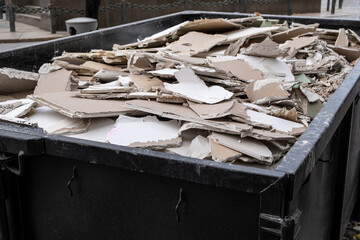 an overloaded dumpster waste container, with construction waste and drywall plasterboard, debris...