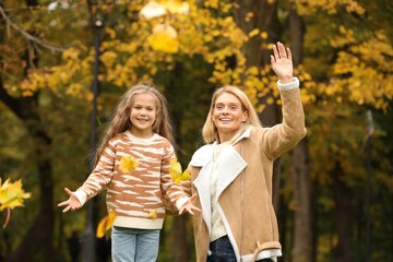 Fototapeta premium Happy mother and her daughter playing with dry leaves in autumn park