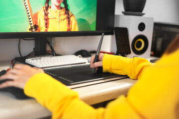 A young girl draws on a PC using a graphics tablet in comfortable home office. Close-up of hand...