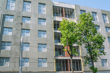 Plastering of thermal insulation surfaces on the facade of the building . Work on the cladding of the building. Trees grow in front of the house under construction. Installing windows.