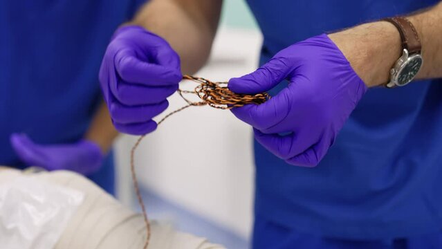 Male hands in latex gloves untangle the black and yellow wire of equipment. Preparation for the neuromonitoring of a patient. Close up.