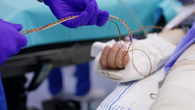 Attaching the patient to the neuromonitoring equipment. Gloved hands untangle the wires near patient's hand.