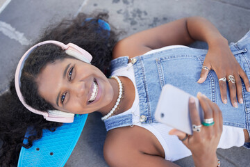 Portrait, phone and music with a black woman skater lying on her board at a skatepark from above....