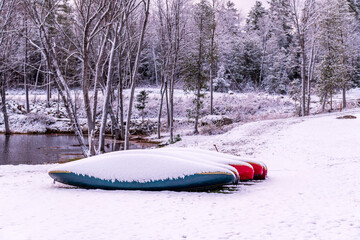 canoes on a river bank under a layer of fresh fallen snow with trees in the background room for text shot in the ottawa valley eastern ontario