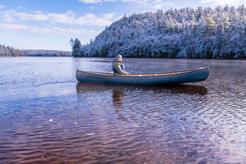 young woman paddling a green canoe solo  on a river with trees clad in freshly fallen snow in the...
