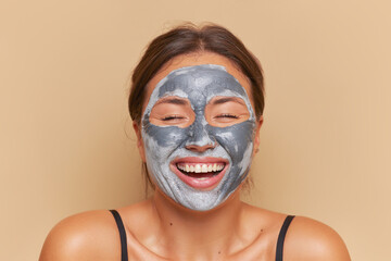 Close-up of smiling young woman isolated over peach background, face cosmetics, clay facial mask, skincare routine concept, copy space