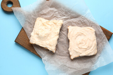 Wooden board of tasty toasts with cream cheese on blue background