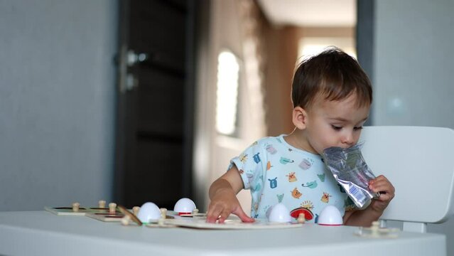 Toddler boy sitting at the desk with the toys. Kid drinking juice from the pack. Blurred backdrop.