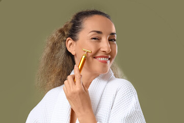 Obraz premium Beautiful mature woman using face massage roller on khaki background