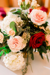 A beautiful floral arrangement at a wedding reception with pink and red roses and green leaves. 