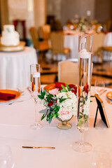 An elegant wedding reception with a floral centerpiece nad floating candle vases, and a wedding cake in the background