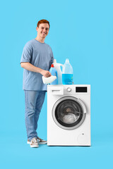 Young man with detergent near washing machine on blue background