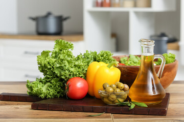 Jug with oil, lettuce, olives and vegetables on table in kitchen