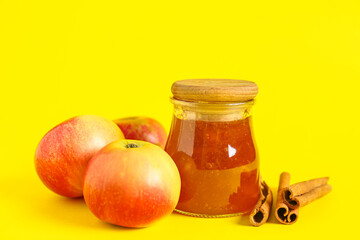 Jar of sweet apple jam with cinnamon on yellow background