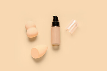 Bottle of makeup foundation with sponges on beige background