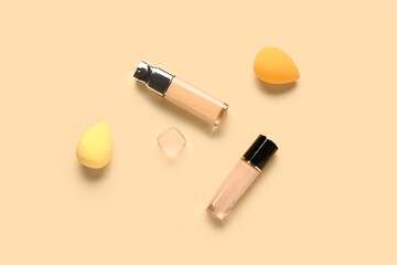 Bottles of makeup foundation with sponges on beige background