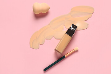 Bottle of makeup foundation with sample, brush and sponge on pink background