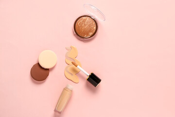 Bottle of makeup foundation with sample, highlighter and sponges on pink background