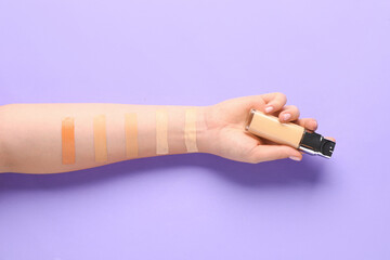 Female hand with bottle of makeup foundation and samples on purple background