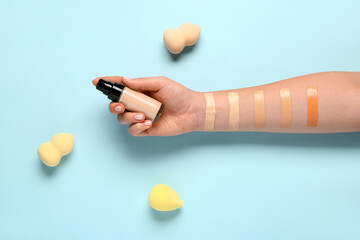 Female hand with bottle of makeup foundation, sponges and samples on blue background