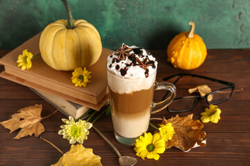 Glass cup of tasty pumpkin latte with star anise and beautiful flowers on wooden table