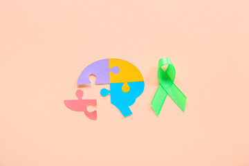 Colorful puzzle pieces in shape of brain with green awareness ribbon on pink background. Mental Health Day