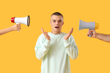 Shocked teenage boy and hands with megaphones on yellow background