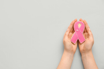 Female hands with cookie in shape of pink ribbon on grey background. Breast cancer awareness concept