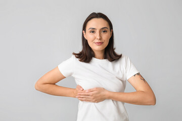 Fototapeta premium Young woman checking her breast on light background. Cancer awareness concept