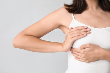 Young woman checking her breast on light background, closeup. Cancer awareness concept