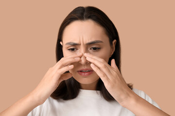 Young woman touching her nose on beige background, closeup