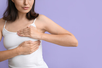 Young woman checking her breast on lilac background, closeup. Cancer awareness concept
