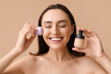 Young woman with makeup sponge and foundation on beige background, closeup