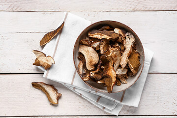 Bowl with tasty dried mushrooms on white wooden background - obrazy, fototapety, plakaty