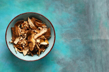 Bowl with tasty dried mushrooms on blue background