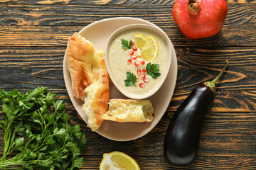 Bowl of tasty baba ghanoush with eggplant and pomegranate on wooden background
